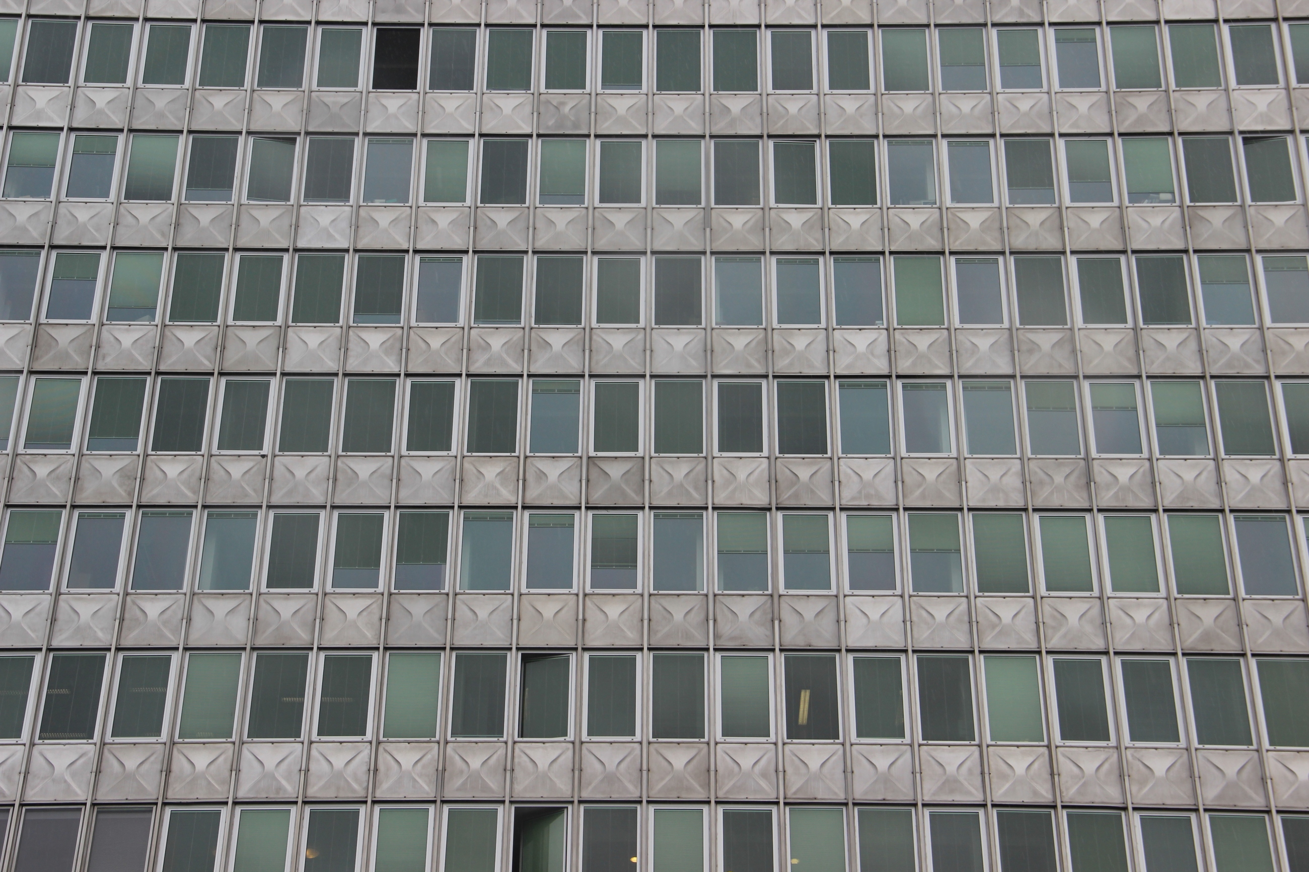 Foto: Graue moderne Fassade mit dunklen Fenstern. Hinter manchen brennt schwaches Neonlicht.