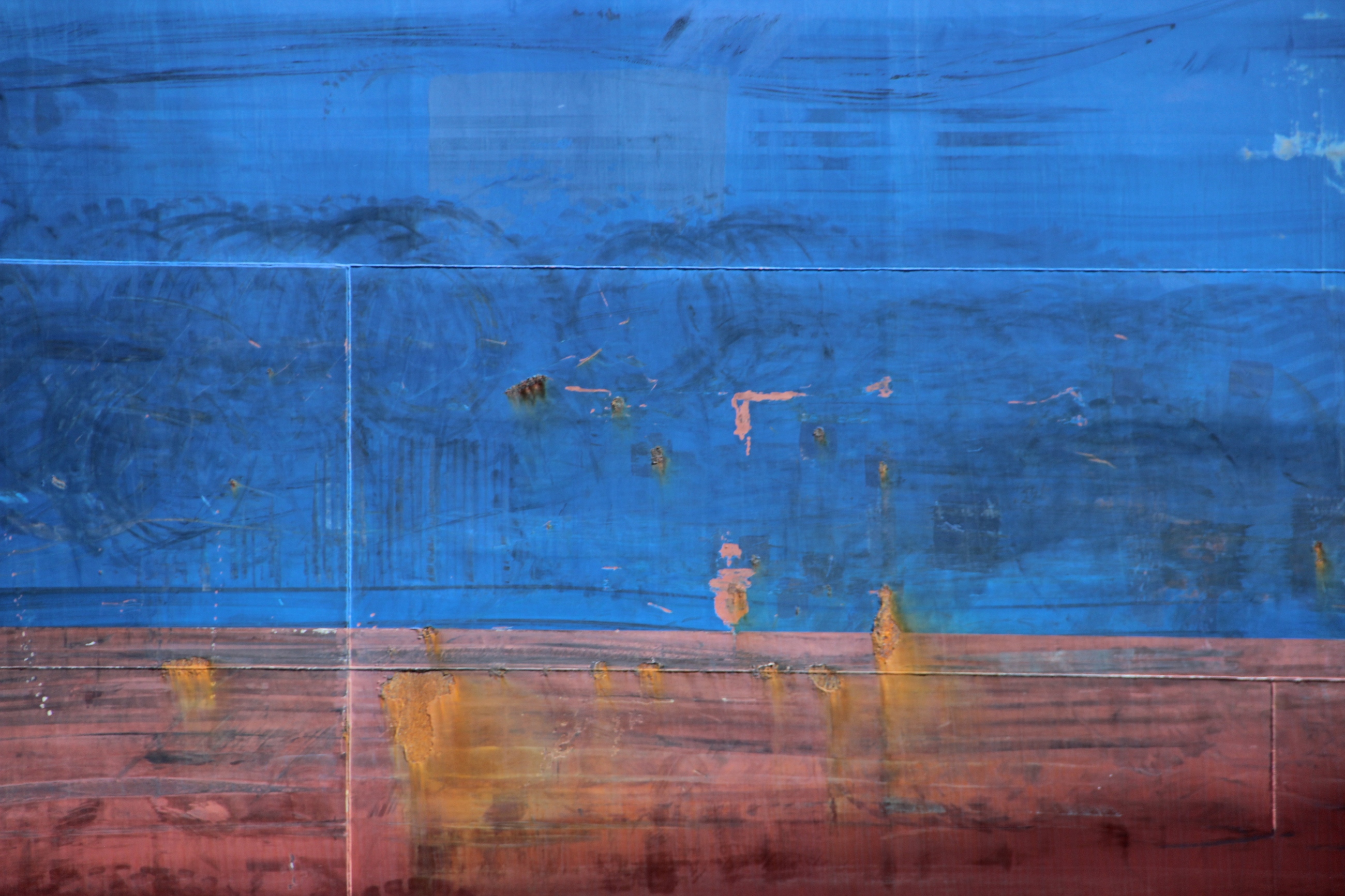 Foto: Blau und rot bemalter Schiffsrumpf mit Rostflecken.